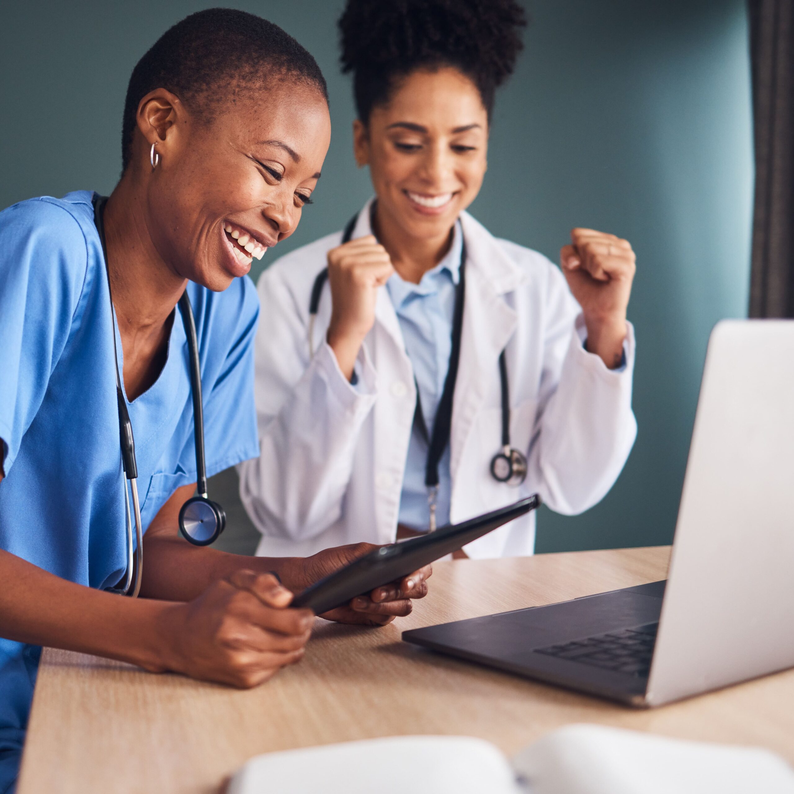 Two healthcare workers celebrate something on a laptop and tablet.